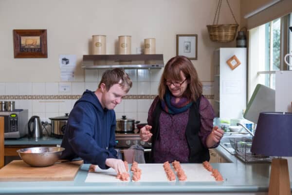 Young Man Making Sausage Rolls with Help from Support Worker